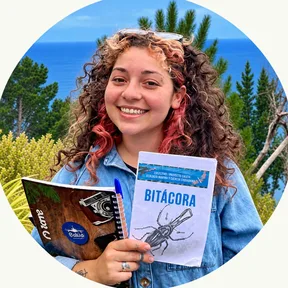 Javiera sonriendo con su bitácora de ecología marina, con árboles y el mar de fondo